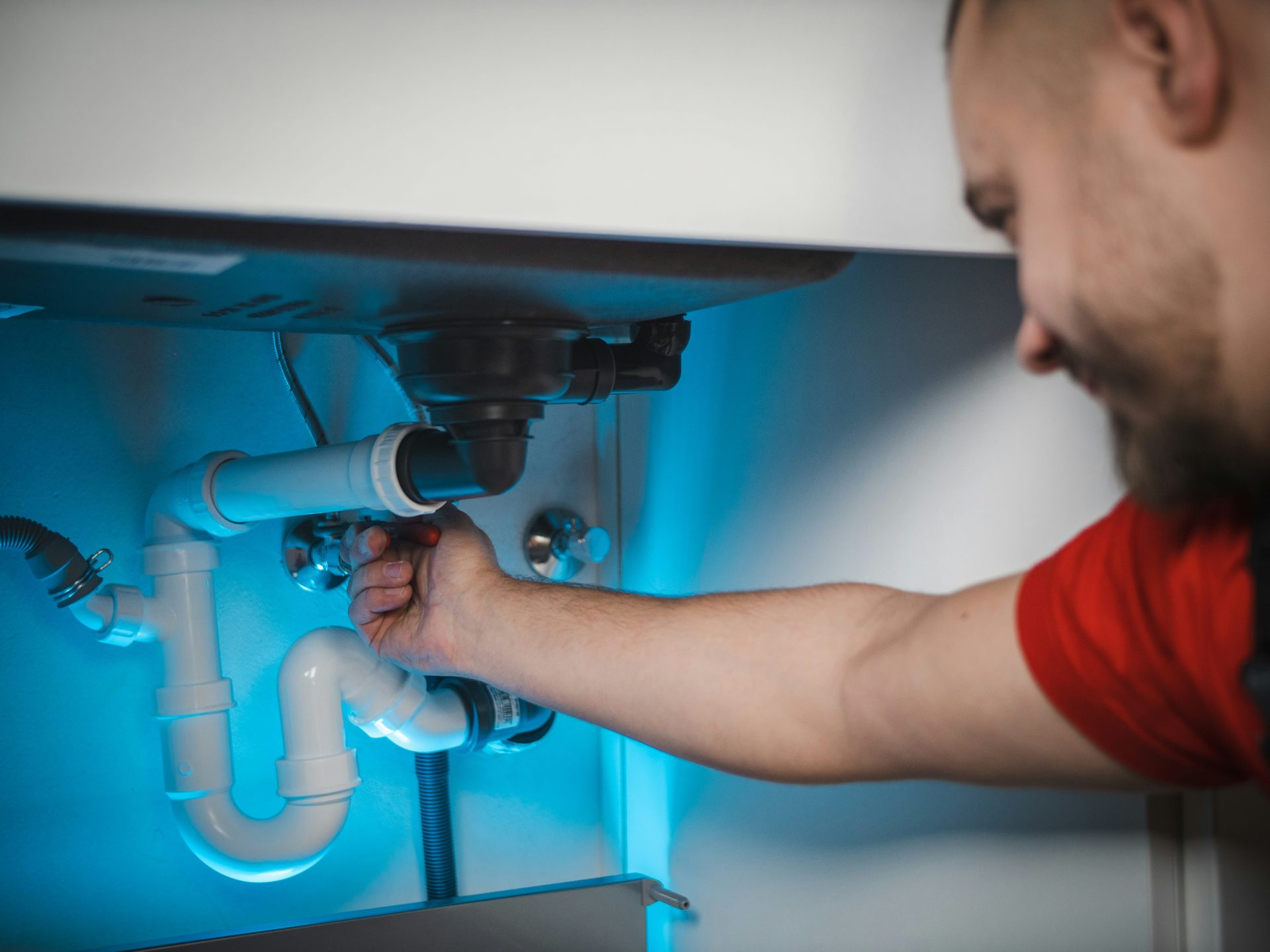 Plumber repairing waste pipework under a kitchen sink